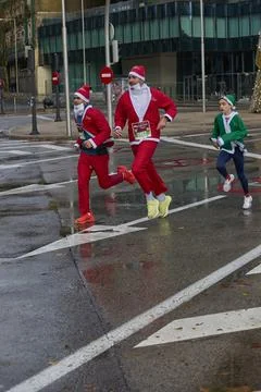 Three runners in Santa and elf costumes running through a city intersection Stock Photos