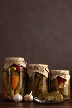 Three rustic jars filled with pickled cucumbers, garlic, peppers, and spices. Stock Photos