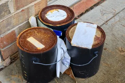 Three rusty paint cans sit outside on the concrete Stock Photos