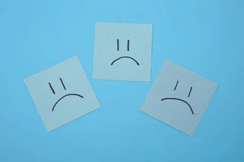 Three sad face sticky notes on blue background Stock Photos