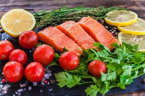 Three salmon steakes with greenery, lemon and cherry tomatoes on the black bo Stock Photos