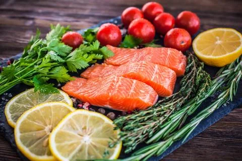 Three salmon steakes with greenery, lemon and cherry tomatoes on the black bo Stock Photos