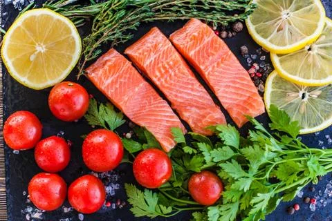Three salmon steakes with greenery, lemon and cherry tomatoes on the black bo Stock Photos