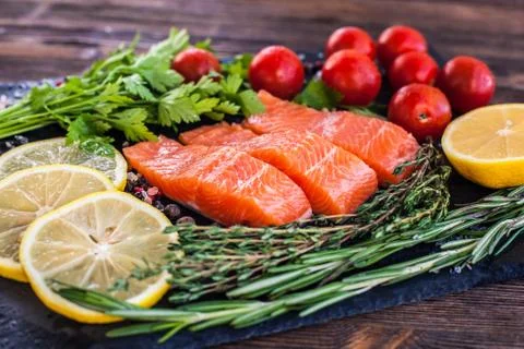 Three salmon steakes with greenery, lemon and cherry tomatoes on the black bo Stock Photos