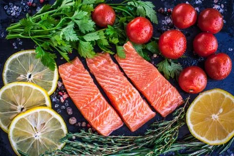 Three salmon steakes with greenery, lemon and cherry tomatoes on the black bo Stock Photos
