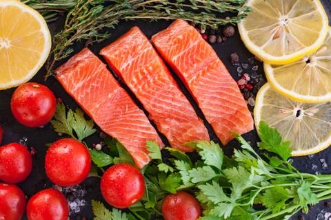 Three salmon steakes with greenery, lemon and cherry tomatoes on the black bo Stock Photos