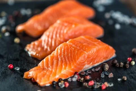 Three salmon steakes with pepper and salt grains on the black board Stock Photos