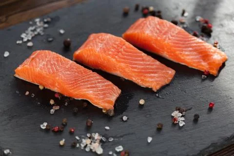 Three salmon steakes with pepper and salt grains on the black board Stock Photos