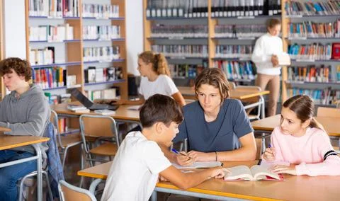 Three schoolchildren writes synopsis in an exercise book from the textbook Stock Photos
