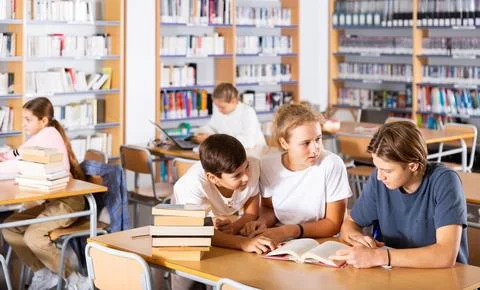 Three schoolchildren writes synopsis in an exercise book from the textbook Stock Photos