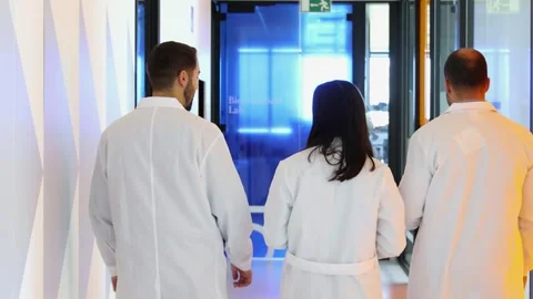 Three Scientists, seen from behind, walking in corridor of modern laboratory Stock Footage 296884927
