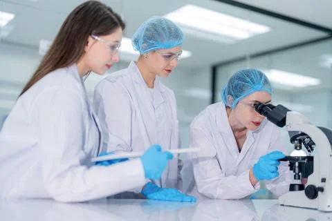 Three scientists work together in a laboratory looking through a microscope.. Stock Photos