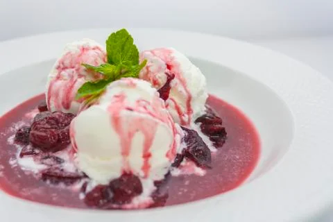 Three scoops of delicious ice cream with flowing plum jam and a sprig of mint Stock Photos