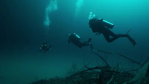 Three scuba divers swimming together in the dark, clear water of a freshwater Stock-Footage 332002148