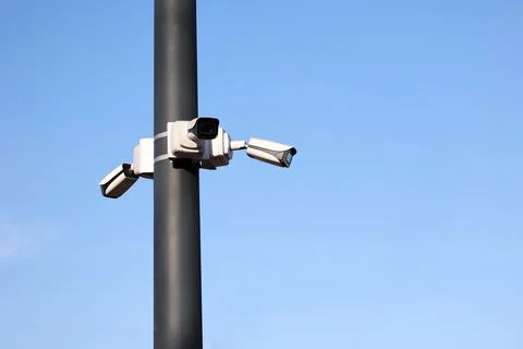 Three security cameras on a pole against blue sky Stock Photos