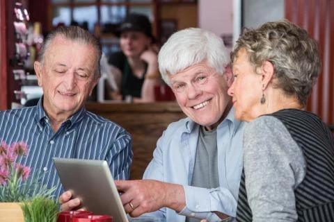 Three senior citizens using tablet computer in bistro Stock Photos