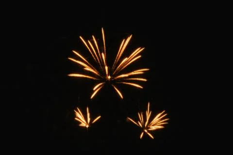 Three separated golden fireworks explosions glow against a deep black sky, .. Stock Photos
