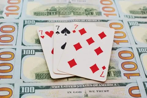 Three sevens from a deck of playing cards lie on spread out hundred-dollar bi Stock Photos