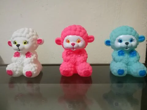 Three sheep dolls of different colors placed in a line and their reflections Stock Photos