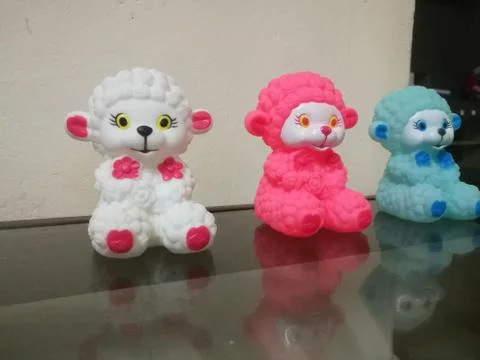 Three sheep dolls of different colors placed in a line and their reflections Stock Photos