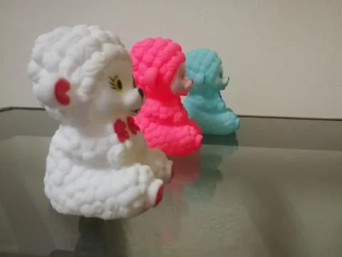 Three sheep dolls of different colors placed in a line and their reflections Stock Photos