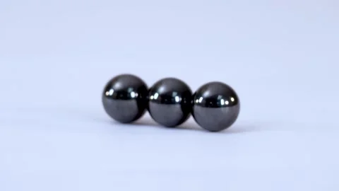 Three Shiny Magnetic Spheres Attracting and Connecting on a White Surface Stock Footage 328619408