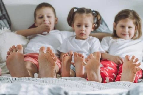 Three siblings lie on bed with bare feet. Focus on legs of the children. Two Stock Photos