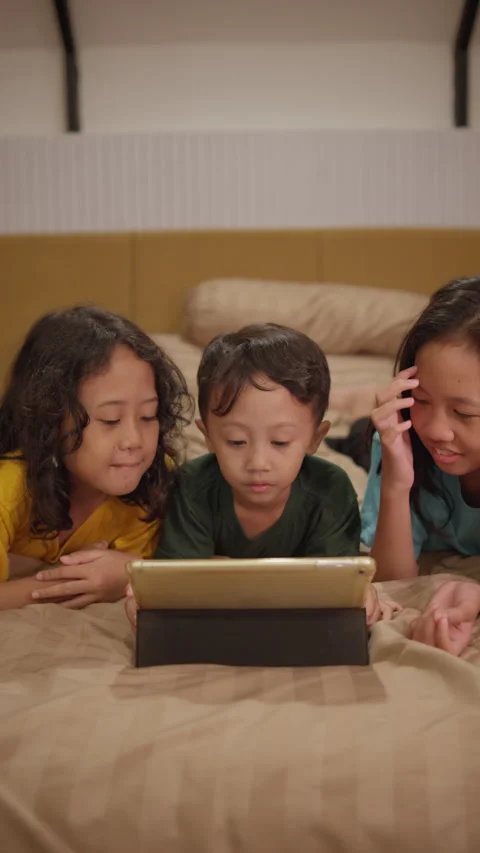 Three siblings lie on their stomachs side by side on a bed Stock Footage 339767268