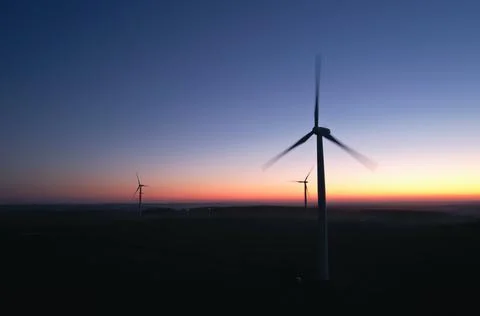 Three silhouettes of rotating propellers of wind turbines against the background Stock Photos
