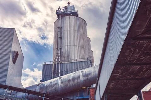 Three silos and a large pipe of a factory with dramatic sky Foto stock