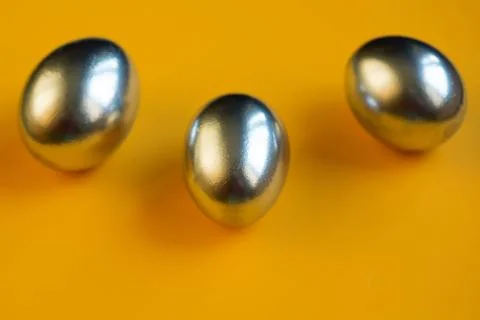 Three silver eggs lie on a yellow background Stock Photos