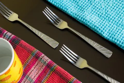 Three silver forks between blue and multicolor napkins with yellow cup. Stock Photos