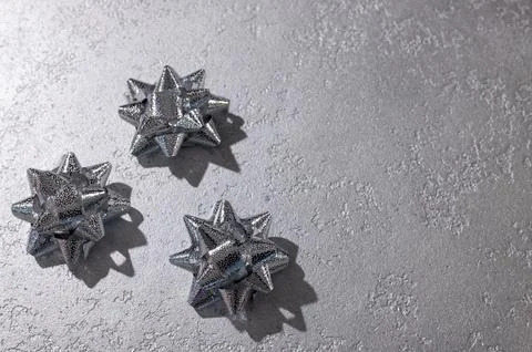 Three silver gift bows casting dramatic shadows on textured gray background.. Фото