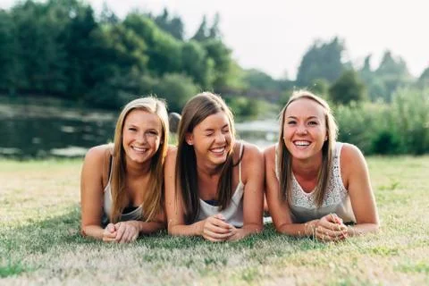 Three sisters laying down in grass smiling and laughing harder Stock Photos