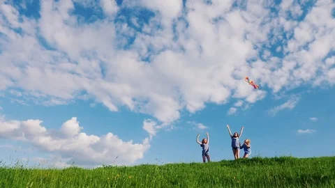 Three sisters playing with a kite on a green hill. Copyspace composition Stock Footage 76047886