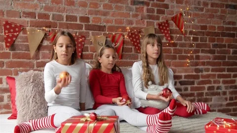 Three sisters sitting on the bed in soft pajamas and playing with red apples Stock Footage 96416104