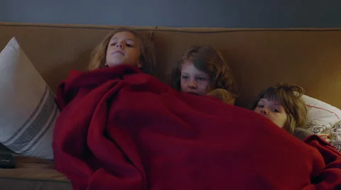Three sisters sitting on a couch sharing a blanket and watching TV Stock Footage 55765663