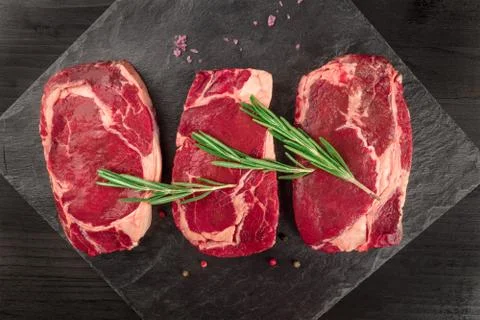Three slices of raw meat on black with seasoning Foto stock