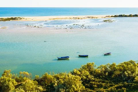 Three small boats float on calm turquoise waters near a sandy shoreline. Stock Photos