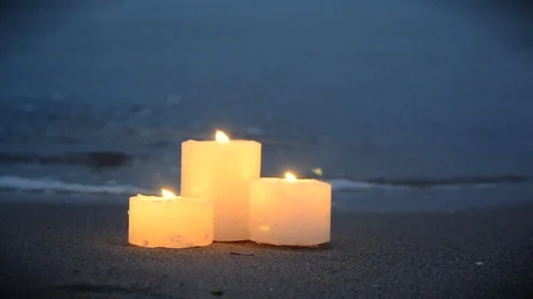 Three small candles on sandy beach near sea ocean waves burning Stock Footage 123388084