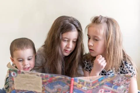 Three small children read a large book. Two sisters and a brother. Light back Stock-Fotos