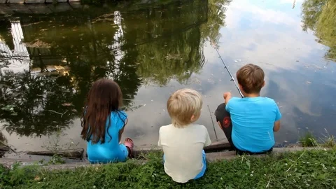 Three small children sit on the shore of the pond and go fishing Stock Footage 92633654