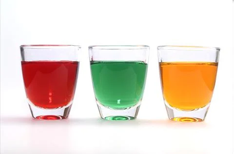 Three small clear glass tumbler with three colour liquids. Stock Photos