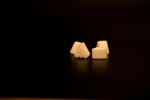 Three small heart and triangle shaped sugar pieces on a dark reflective surface Stock Photos