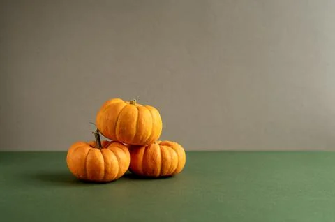 Three small orange pumpkins stacked on a green surface. The background is a Stock Photos