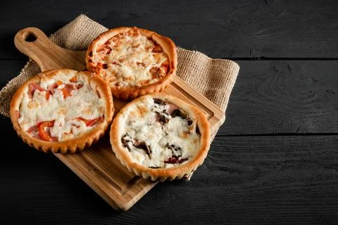 Three small pizzas on a cutting board on a black wooden background. With a .. Stock Photos