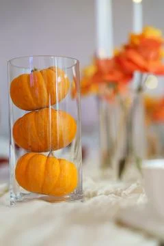 Three small pumpkins are stacked inside a clear glass vase. Flowers and candl Stock-Fotos