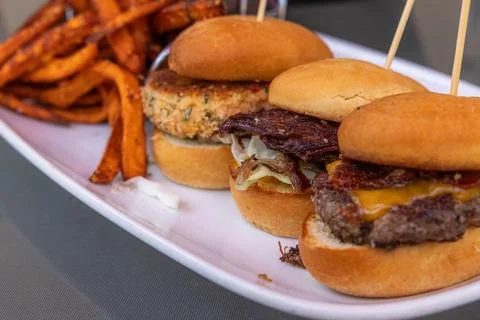 Three small sliders with different ingredients on buns, with a side of fries Stock Photos