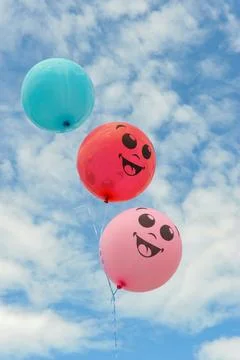 Three smiley balls against a background of blue sky with clouds. Stock Photos