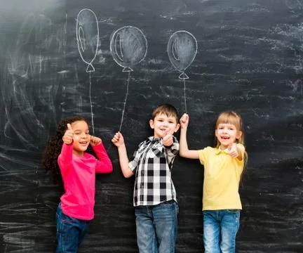 Three smiling children with thumbs up keeping imaginaru drawn balloons Foto stock